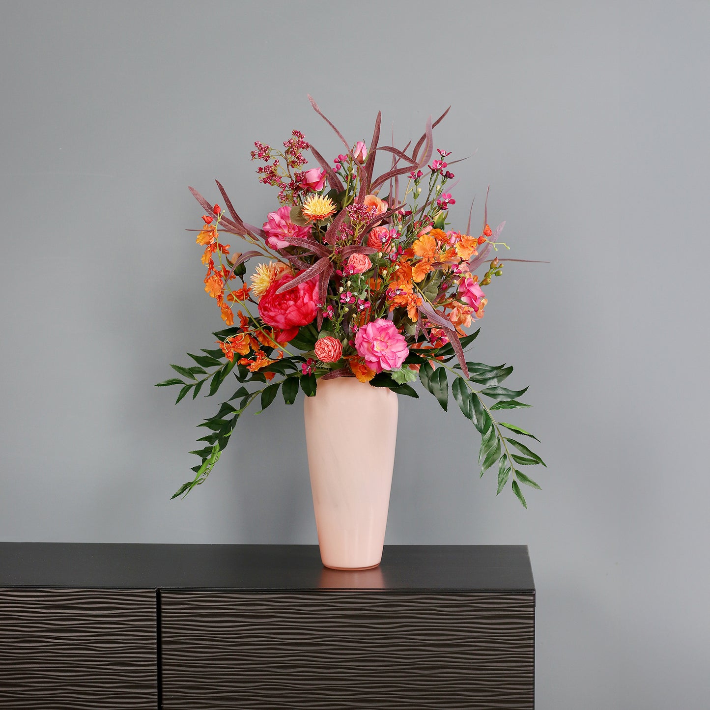 Künstlicher Blumenstrauß Flower Cocktail von Lumisa’s Choice in kräftigen Farben in apricot farbener Vase als moderne Dekoration vor grauer Wand.