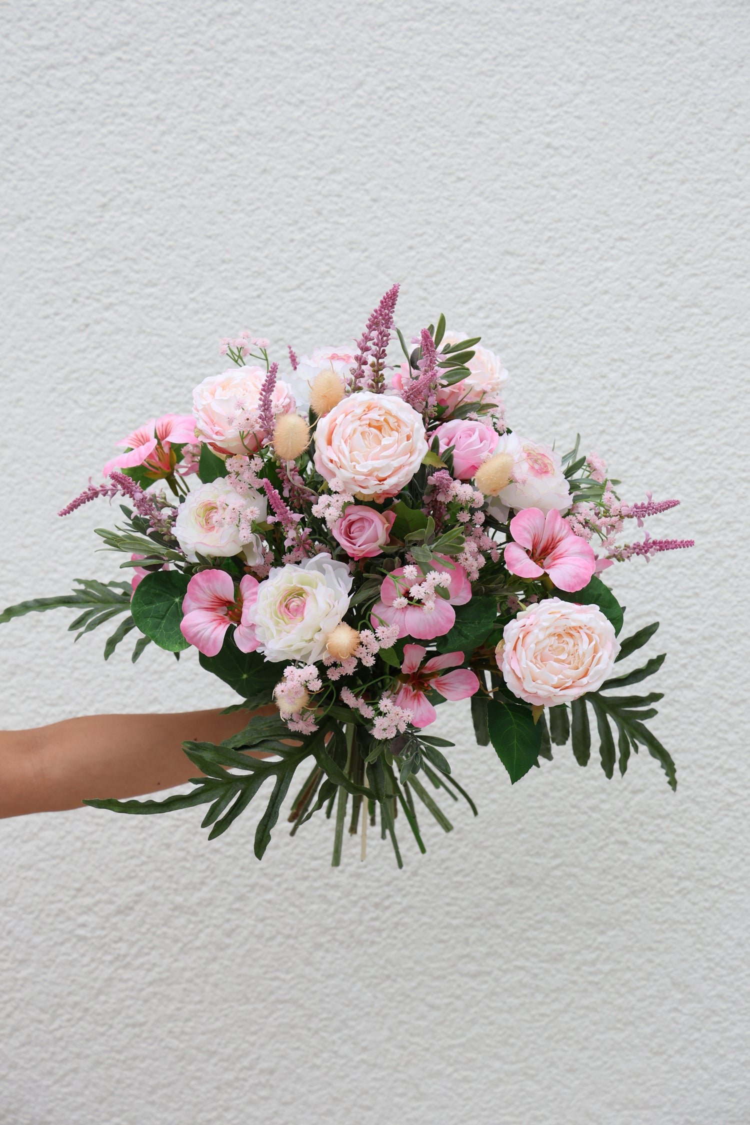Künstlicher Blumenstrauß Sweet Cotton Candy von Lumisa’s Choice in zarten Pastelltönen wird von Person vor einer Wand gehalten.