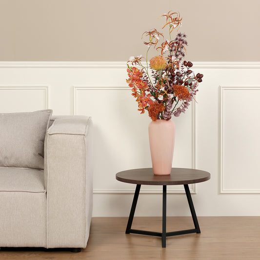 Künstlicher Blumenstrauß African Sunset von Lumisa’s Choice in warmen Farben in apricot farbene Vase als stilvolle Dekoration neben hellem Sofa.