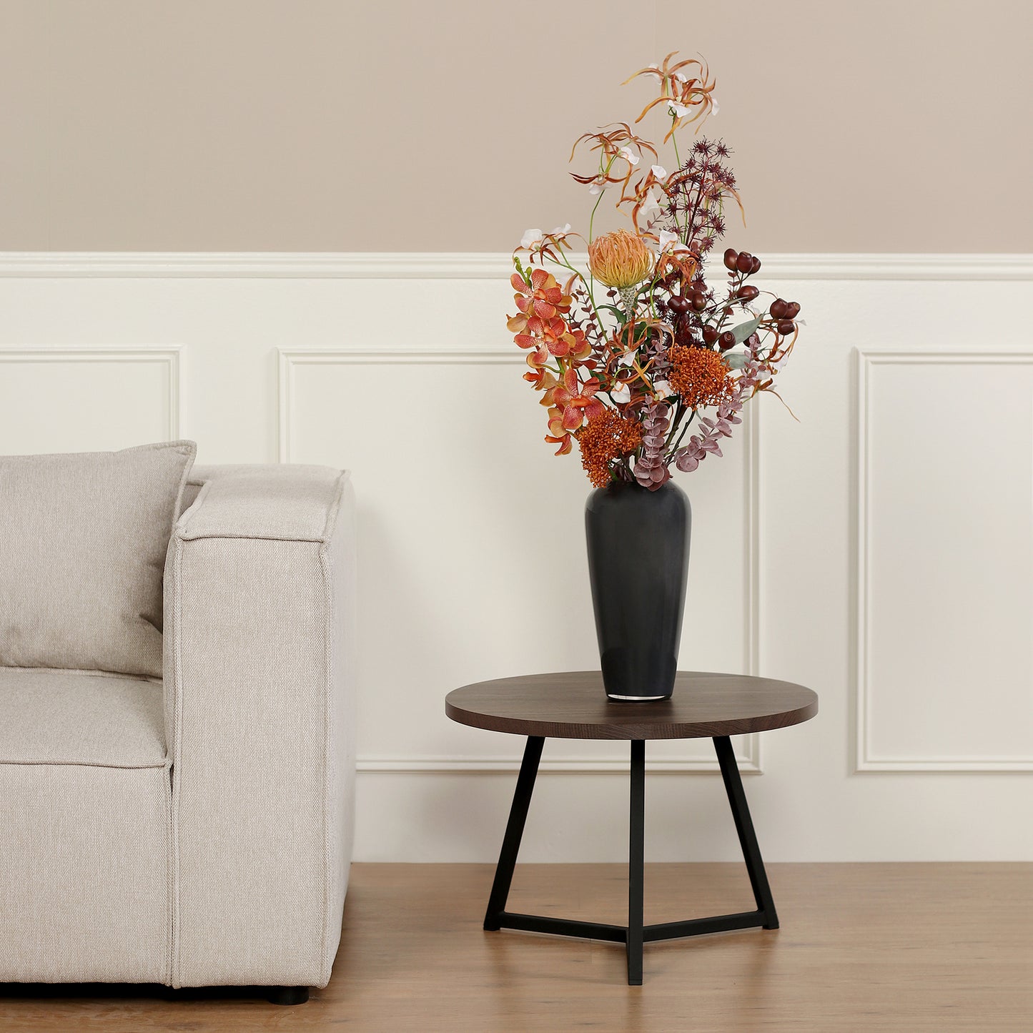 Künstlicher Blumenstrauß African Sunset von Lumisa’s Choice in warmen Farben in schwarzer Vase als stilvolle Dekoration neben hellem Sofa.