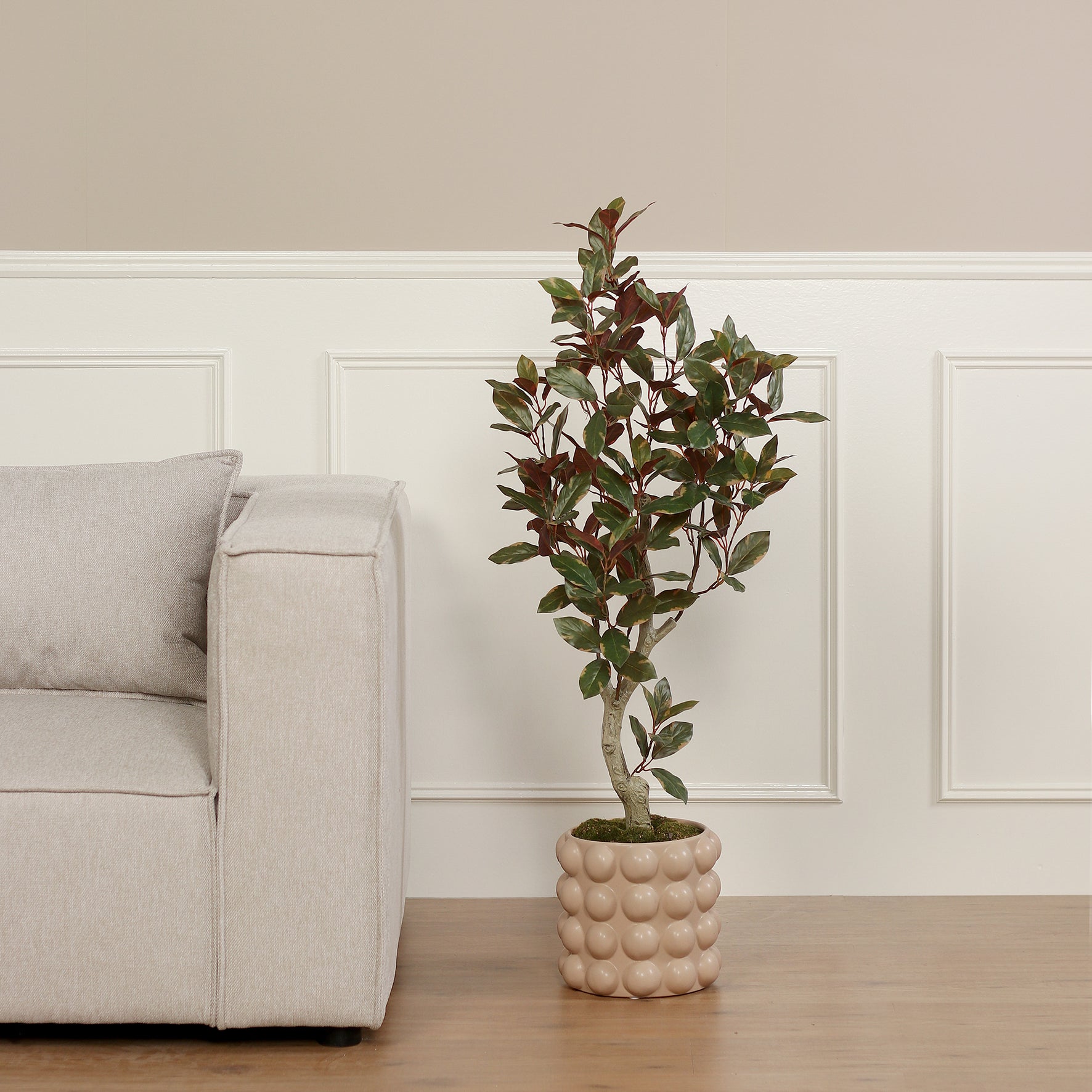 Künstliche Grünpflanze Carpensia von Lumisa’s Choice in beigem Bubble-Keramiktopf neben Sofa.