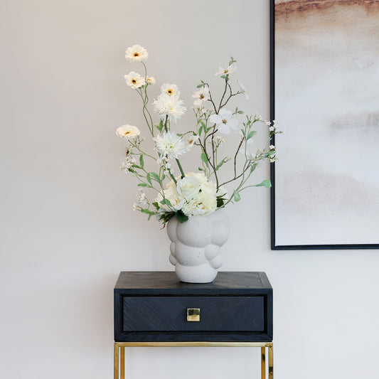 Künstlicher Blumenstrauß Flower Bubble von Lumisa’s Choice mit weißen Blüten in Bubble-Vase auf Beistelltisch neben Bild und heller Wand.
