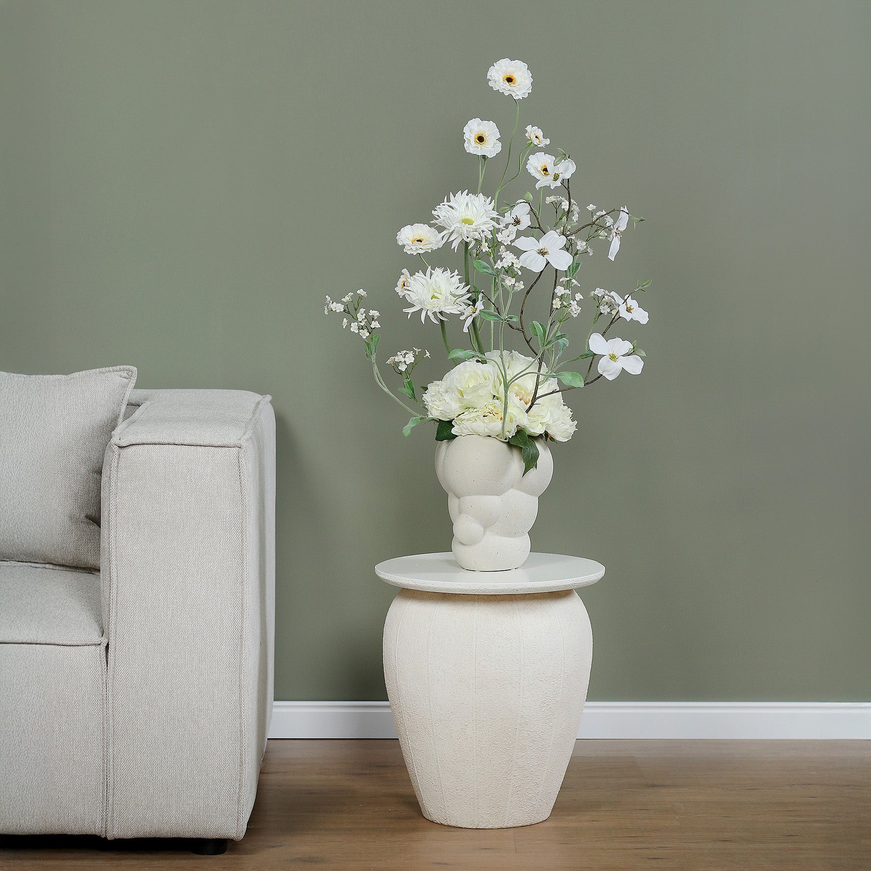 Künstlicher Blumenstrauß Flower Bubble von Lumisa’s Choice mit weißen Blüten in Bubble-Vase auf Beistelltisch neben Sofa im modernen Wohnzimmer.