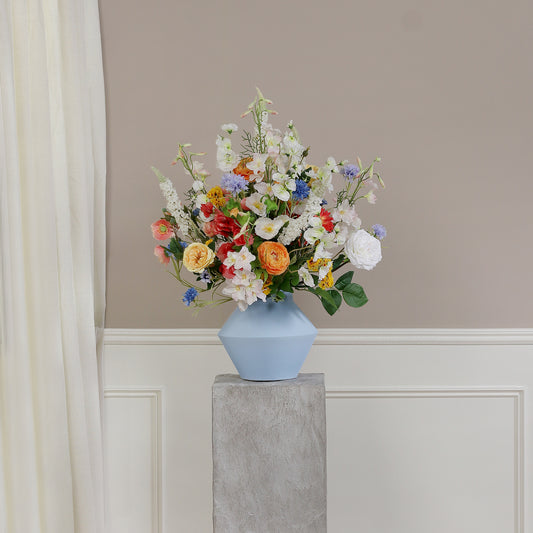 Künstlicher Blumenstrauß Flower Cloud von Lumisa’s Choice in bunten Farben in einer stilvollen blauen Vase auf Podest vor heller Wand.