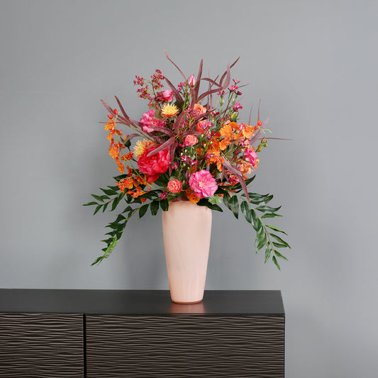 Künstlicher Blumenstrauß Flower Cocktail von Lumisa’s Choice in kräftigen Farben in  apricot farbener Vase als moderne Dekoration vor grauer Wand.