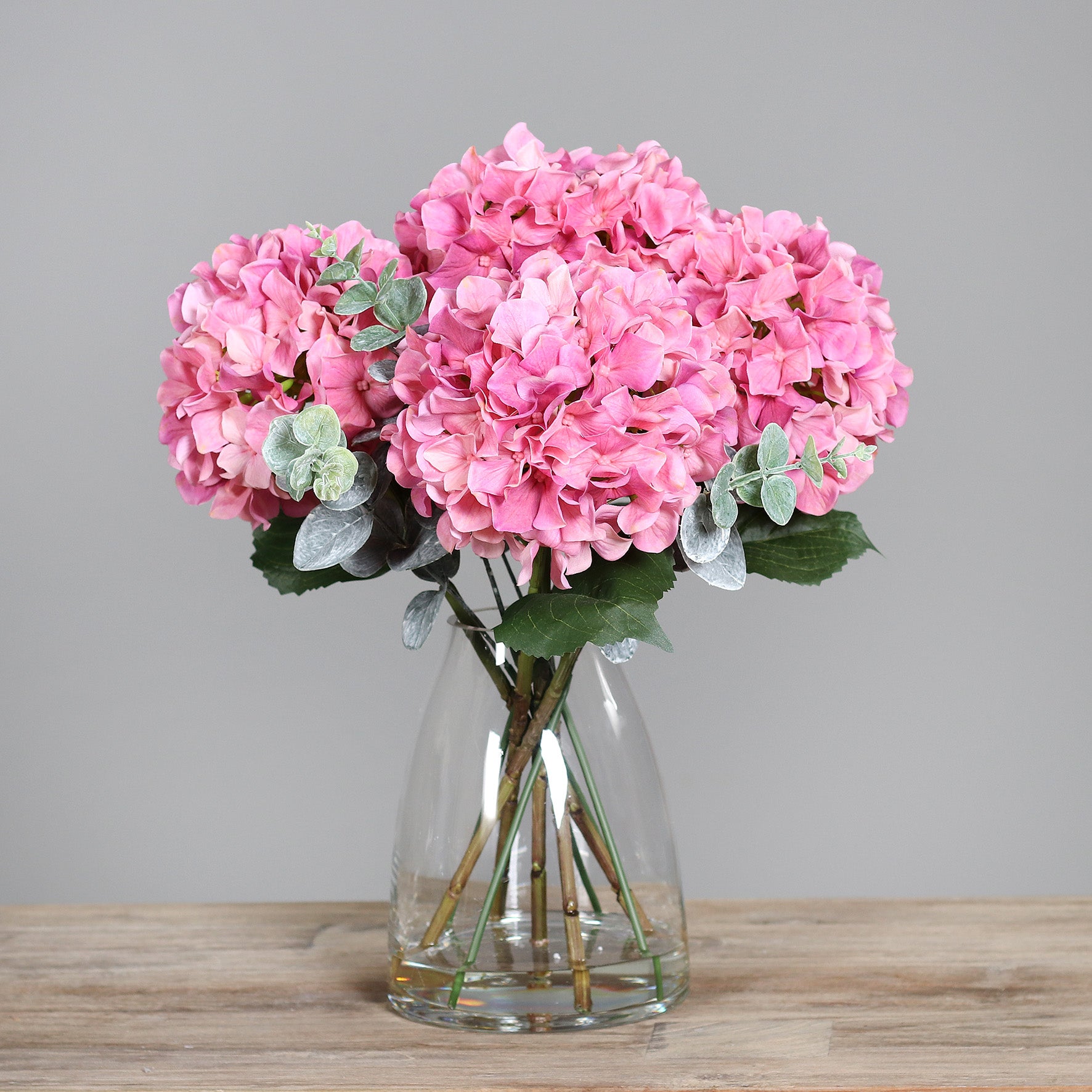 Künstliche pinke Hortensie in Glasvase auf Holztisch
