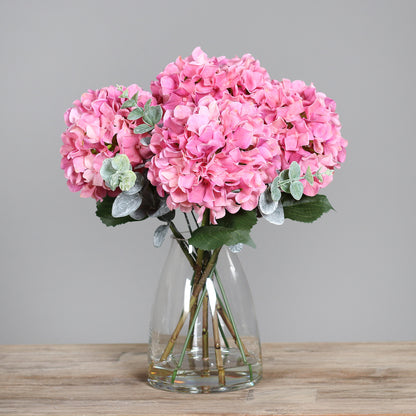 Künstliche pinke Hortensie in Glasvase auf Holztisch