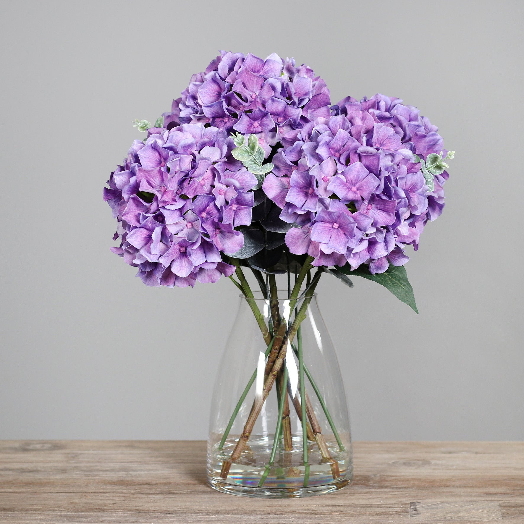 Künstliche violette Hortensie in Glasvase auf Holztisch