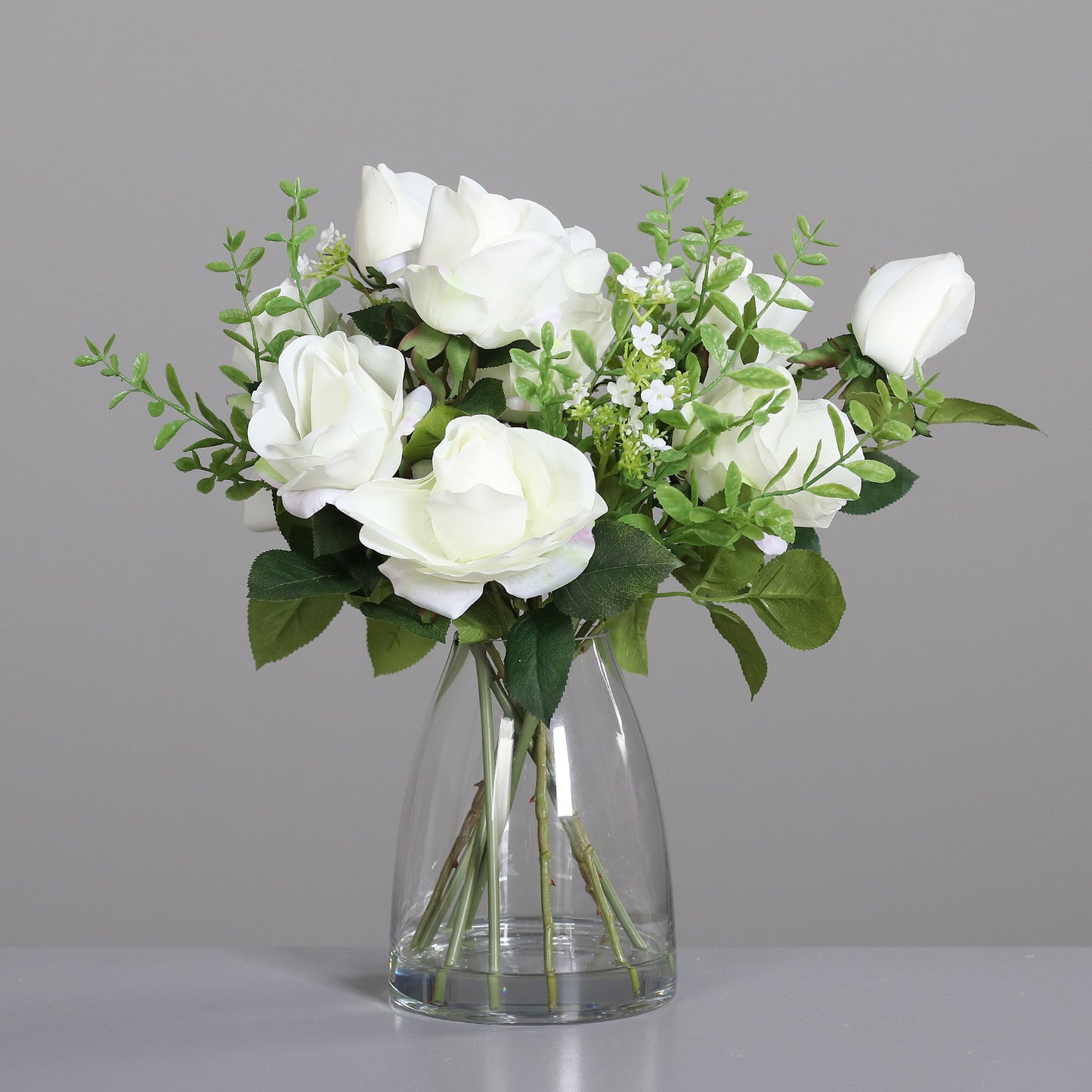 Rosen-Arrangement mit künstlichen weißen Blumen in Glasvase auf Tisch
