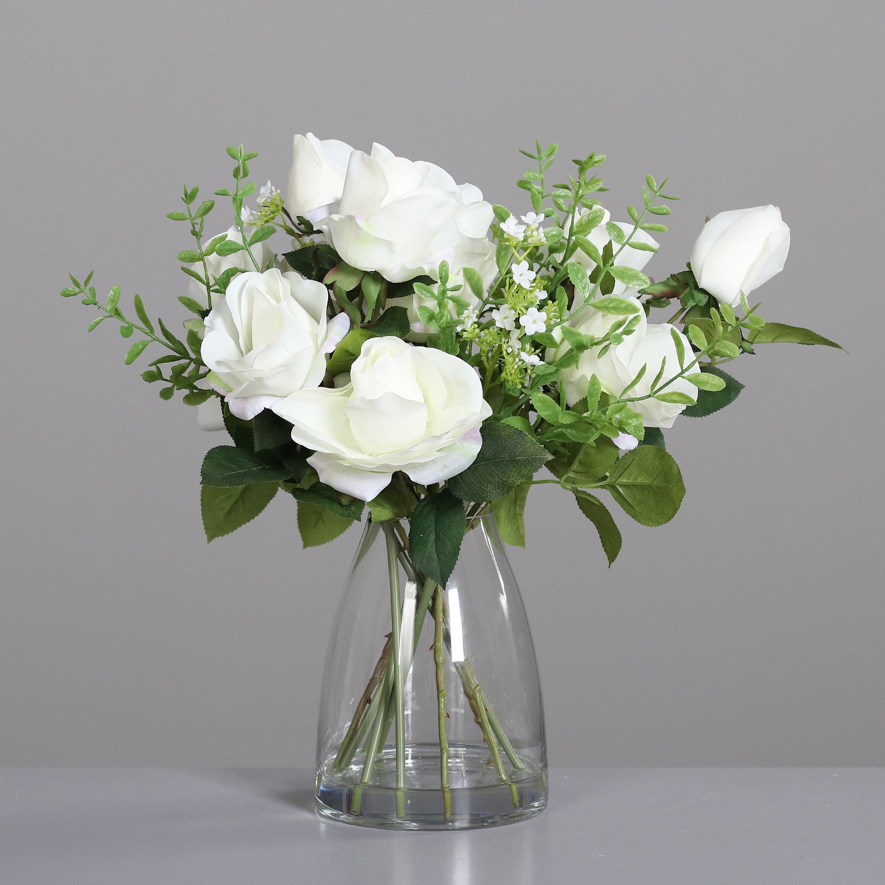 Rosen-Arrangement mit künstlichen weißen Blumen in Glasvase auf Tisch