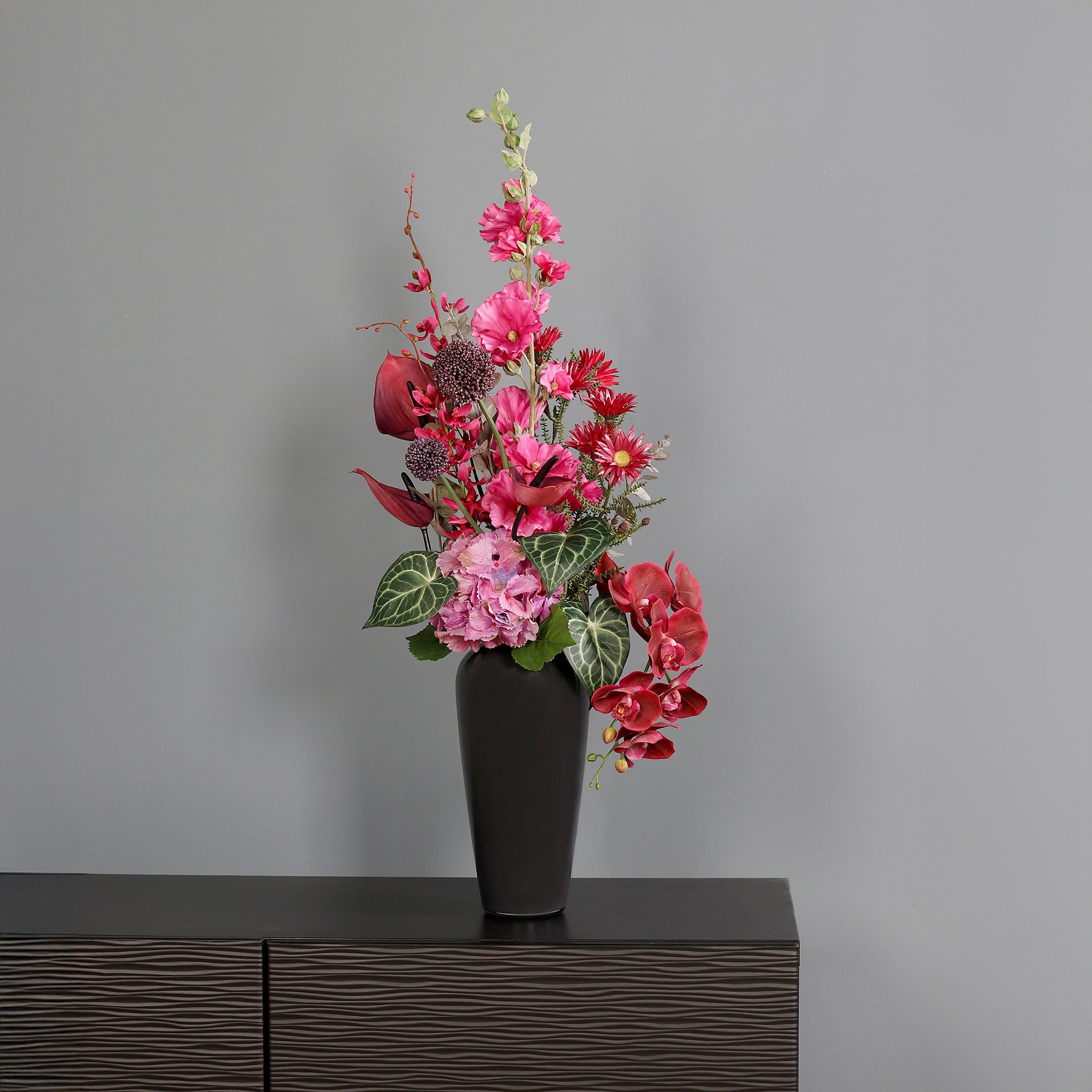 Künstlicher Blumenstrauß Pink Passion von Lumisa’s Choice in kräftigen Pinktönen in schwarzer Vase  als moderne Dekoration vor grauer Wand.