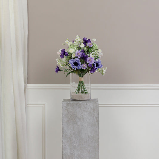 Künstlicher Blumenstrauß Purple Sky von Lumisa’s Choice in Violett- und Weißtönen als elegante Dekoration auf Podest vor heller Wand.