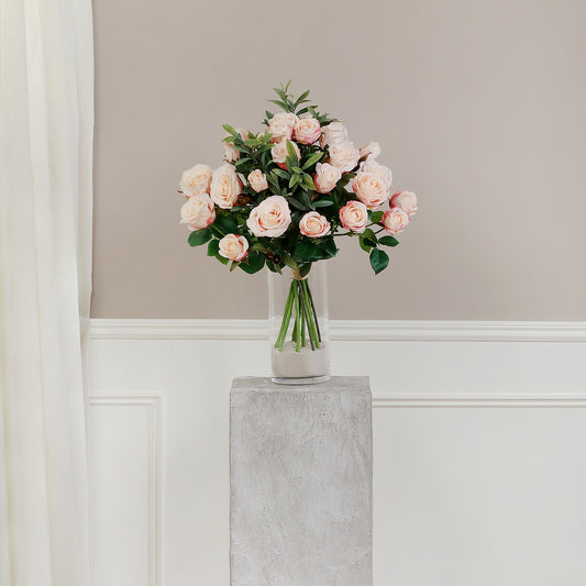 Künstlicher Blumenstrauß Rose Mono Bouquet Apricot von Lumisa’s Choice mit apricotfarbenen Blüten und Olivenzweigen als stilvolle Dekoration auf grauem Sockel vor heller Wand.