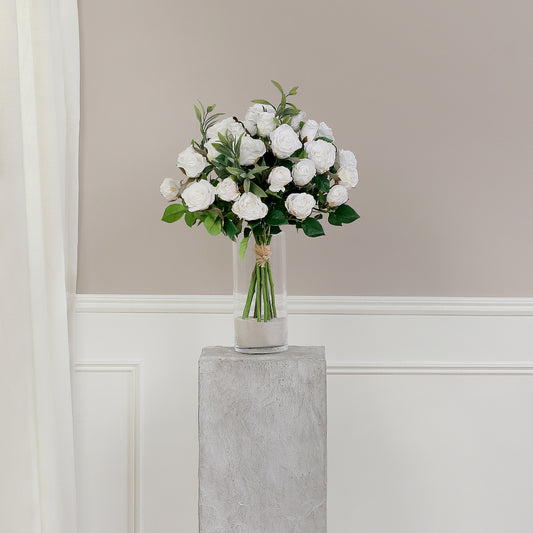 Künstlicher Blumenstrauß Rose Mono Bouquet White von Lumisa’s Choice mit weißen Blüten und Olivenzweigen als elegante Dekoration auf grauem Sockel vor heller Wand.