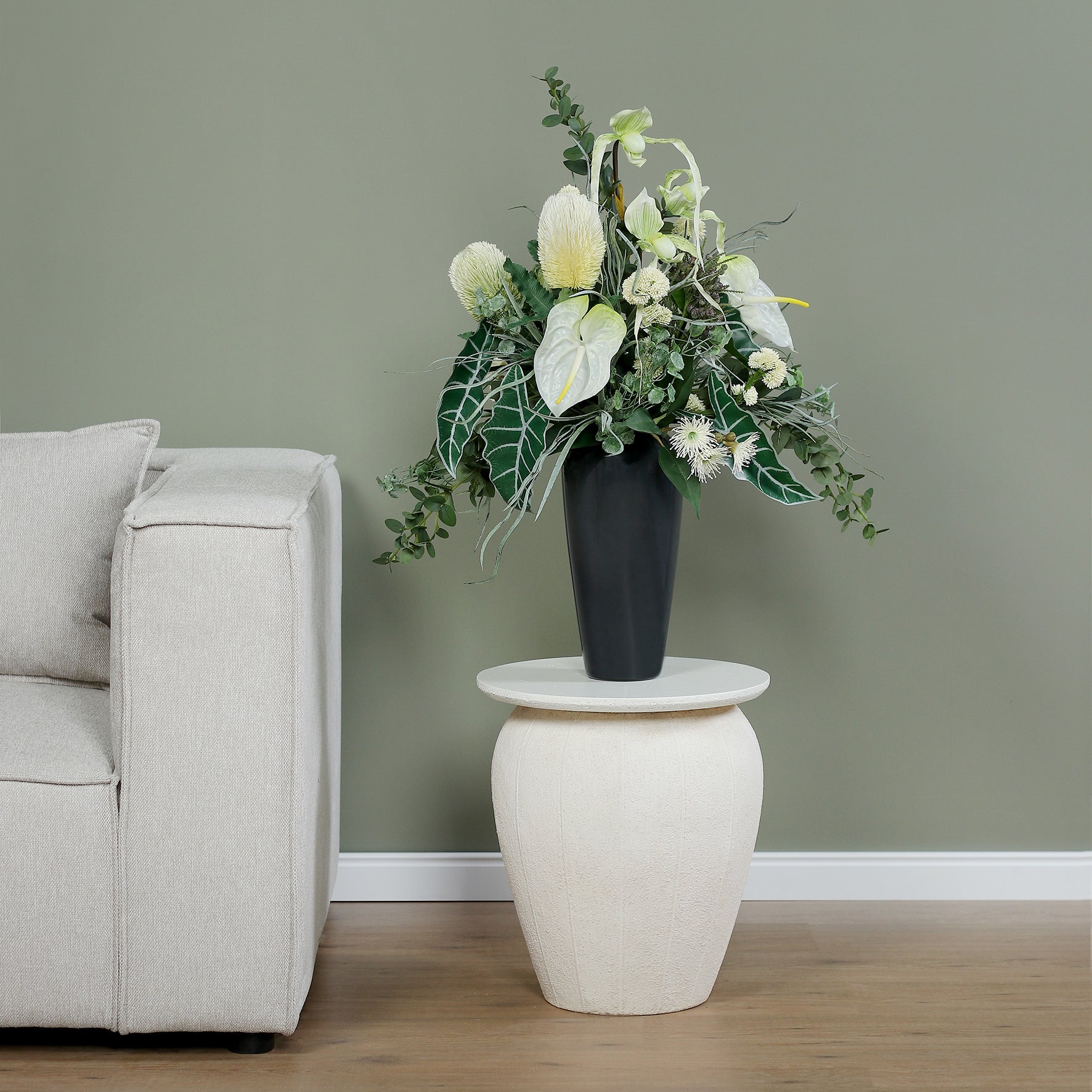 Künstlicher Blumenstrauß Soul of Nature von Lumisa’s Choice in Grün- und Weißtönen in eleganter schwarzer Vase auf Beistelltisch neben hellem Sofa.