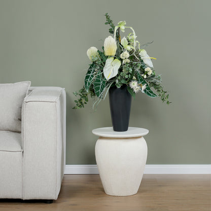 Künstlicher Blumenstrauß Soul of Nature von Lumisa’s Choice in Grün- und Weißtönen in eleganter schwarzer Vase auf Beistelltisch neben hellem Sofa.