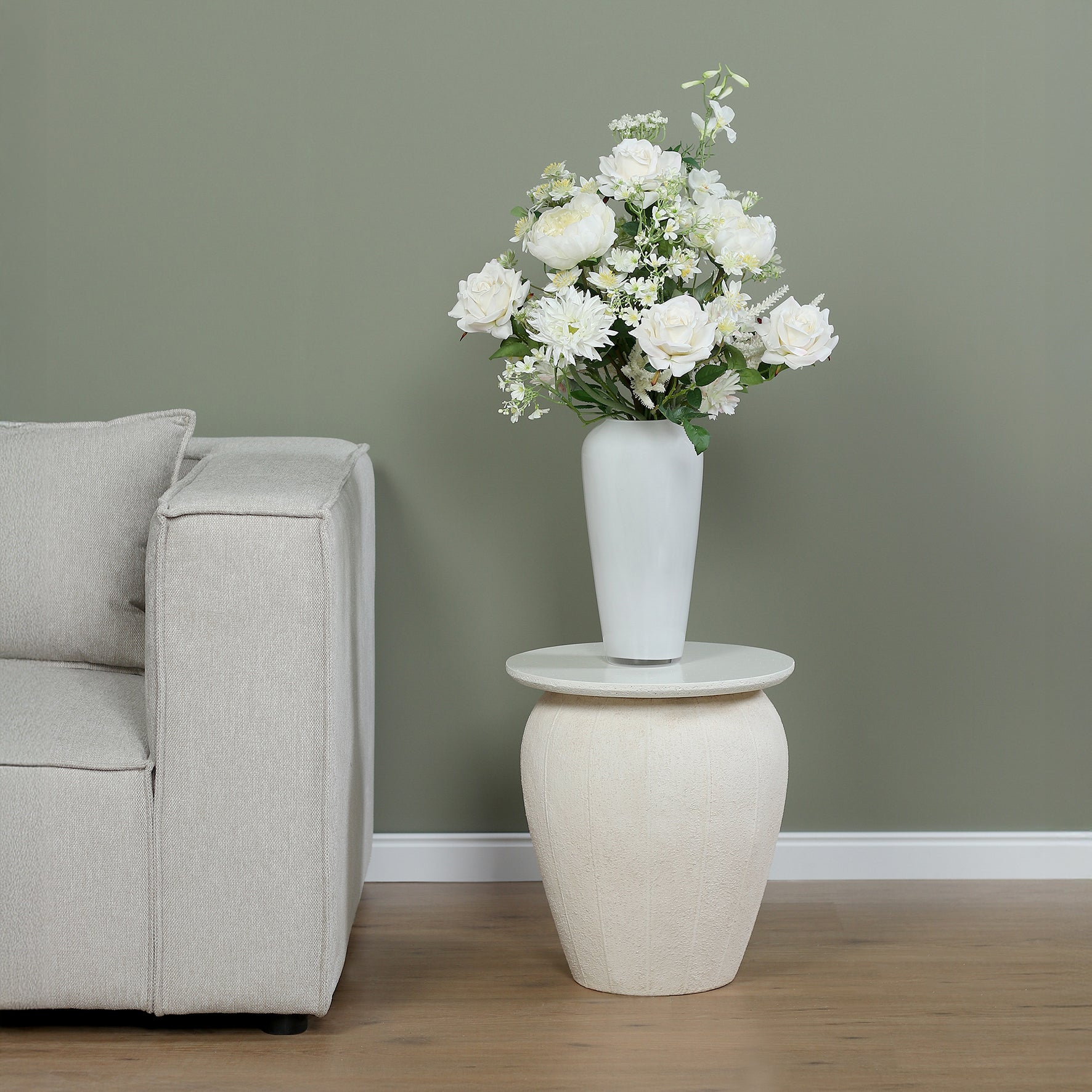 Künstlicher Blumenstrauß White Harmony von Lumisa’s Choice mit weißen Blüten in weißer Vase als stilvolle Dekoration neben hellem Sofa